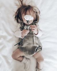 High angle view of toddler girl holding flower on bed