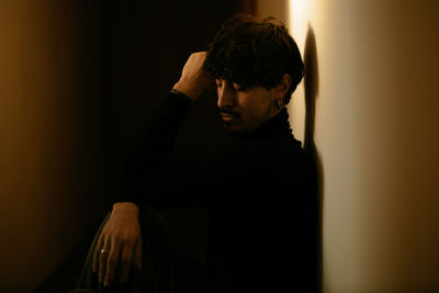 Side view of young man sitting against wall