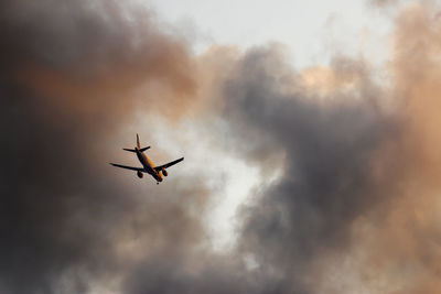 Low angle view of airplane flying against cloudy sky