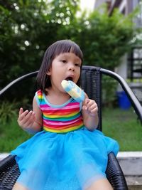 Girl looking away while holding popsicle on chair