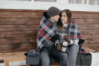 Young couple in love in the woods basking under a blanket. they drink tea from a thermos