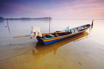 Boat moored in sea against sky during sunset