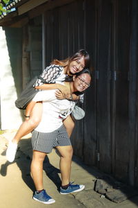 Full length portrait of smiling teenage girl giving piggyback to sister by closed shop