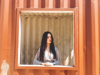 Portrait of young woman standing against curtain