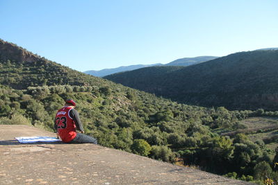 Rear view of woman sitting on mountain against sky