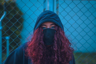 Portrait of beautiful young woman standing by fence