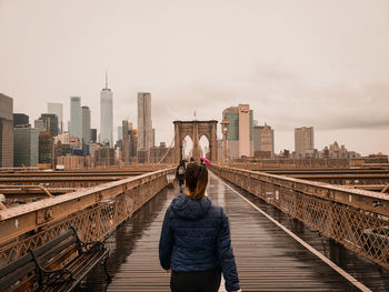 Rear view of woman standing on bridge in city against sky