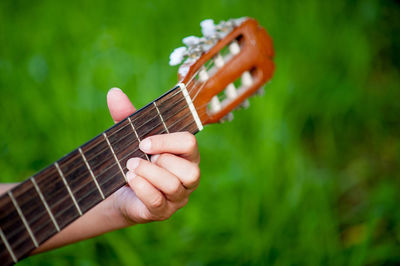 Cropped hand of person playing guitar over field