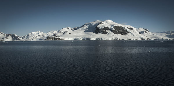 Scenic view of sea and snowcapped mountains against sky