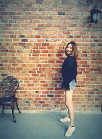 Full length portrait of woman standing against brick wall