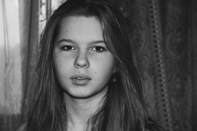 Portrait of young woman with long hair against curtain at home