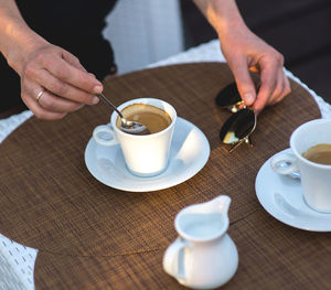 Midsection of person holding sunglasses by milk in jar and coffee cups on table 