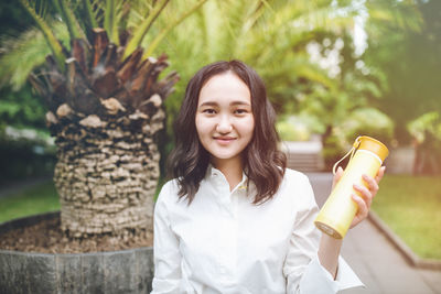 Happy young asian female woman in a park with reusable plastic bottle, smiling. outdoor recreation