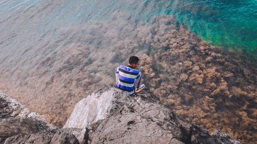 Rear view of man on rock at shore