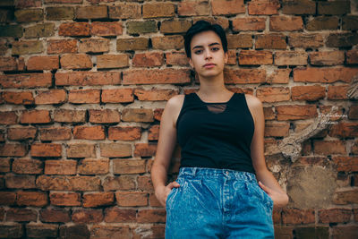 Portrait of young woman standing against brick wall