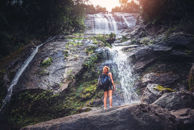 Woman standing on rock against waterfall