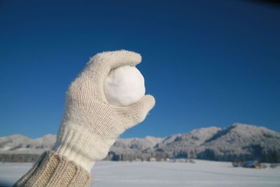 Cropped hand holding snowball against clear blue sky