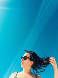 Woman holding wet hair against sky