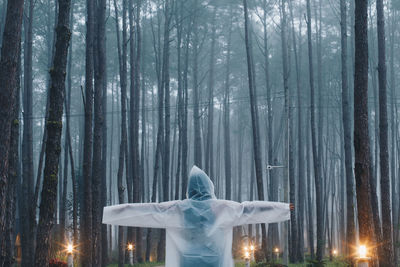 Rear view of woman wearing raincoat while standing by illuminated lights in forest