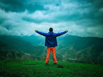 Rear view of man with arms outstretched standing on mountain against cloudy sky