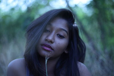 Close-up of thoughtful young woman with plant against trees