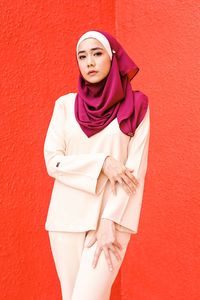 Portrait of young woman wearing hijab while standing against wall