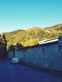 Road by trees against clear blue sky