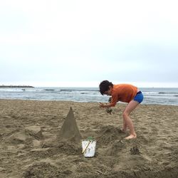 Boy playing with sand at beach against sky