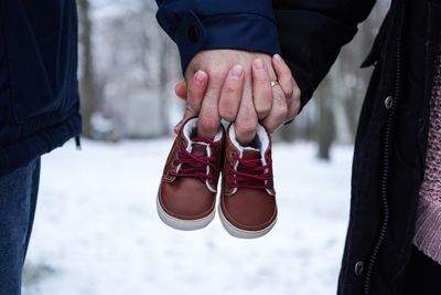 Midsection of couple holding baby booties while standing on field during winter