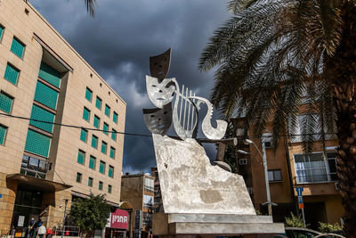 Low angle view of statue by building against sky