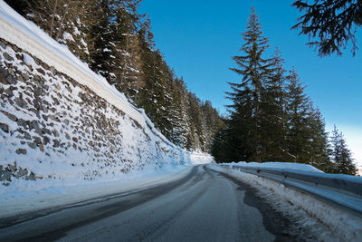 Snow covered road by trees against sky