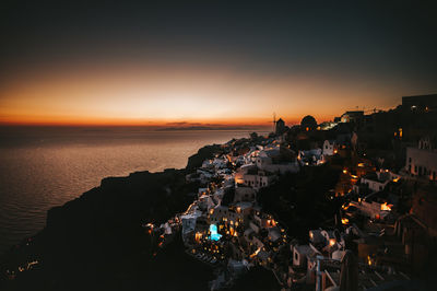 High angle view of illuminated buildings by sea against sky during sunset