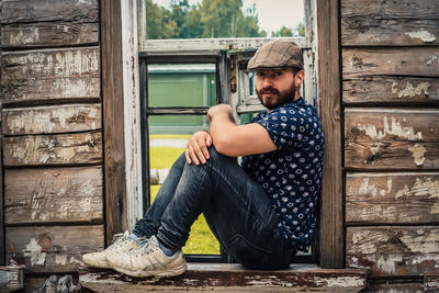 Portrait of young man sitting on wooden window