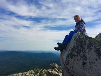 Man sitting on rock against sky