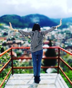 Tilt-shift image of woman with arms outstretched at observation point against townscape