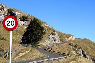 Road sign by mountains against clear blue sky