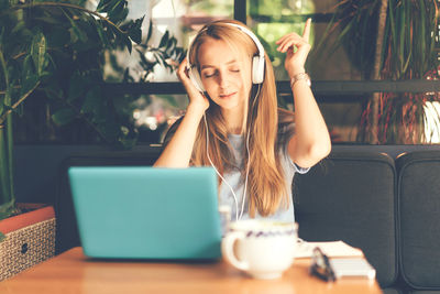 Blonde girl  in a cafe with headphones connected to a laptop listening to music and enjoying dancing