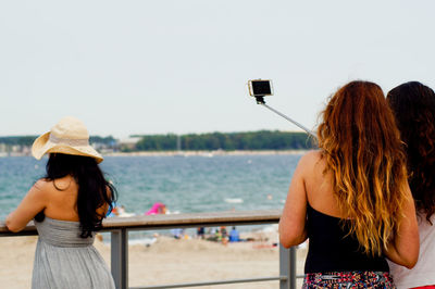 Rear view of friends taking selfie while standing by railing against sea