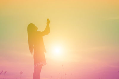 Silhouette woman standing against bright sun during sunset