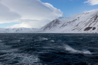 Scenic view of sea and snowcapped mountains against sky