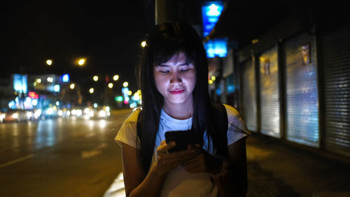 Portrait of woman standing on illuminated mobile phone at night