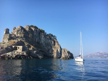 Boat moving on river by rock formation against clear blue sky