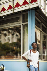 Woman looking away while leaning on cafe wall