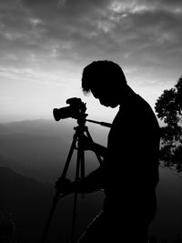 Silhouette man photographing against sky