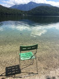 Empty chairs by lake against mountains