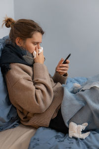 Sick woman using mobile phone while resting on bed