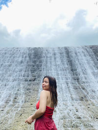 Portrait of young woman standing at beach against sky