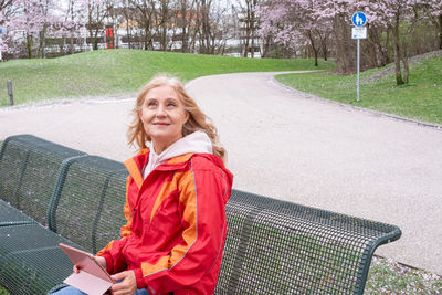 Mature woman sitting on a bench in the park and working on the tablet.