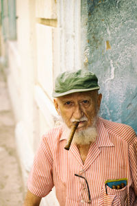 Portrait of senior man wearing cap smoking cigar while sitting outdoors