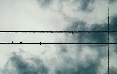 Low angle view of power lines against cloudy sky